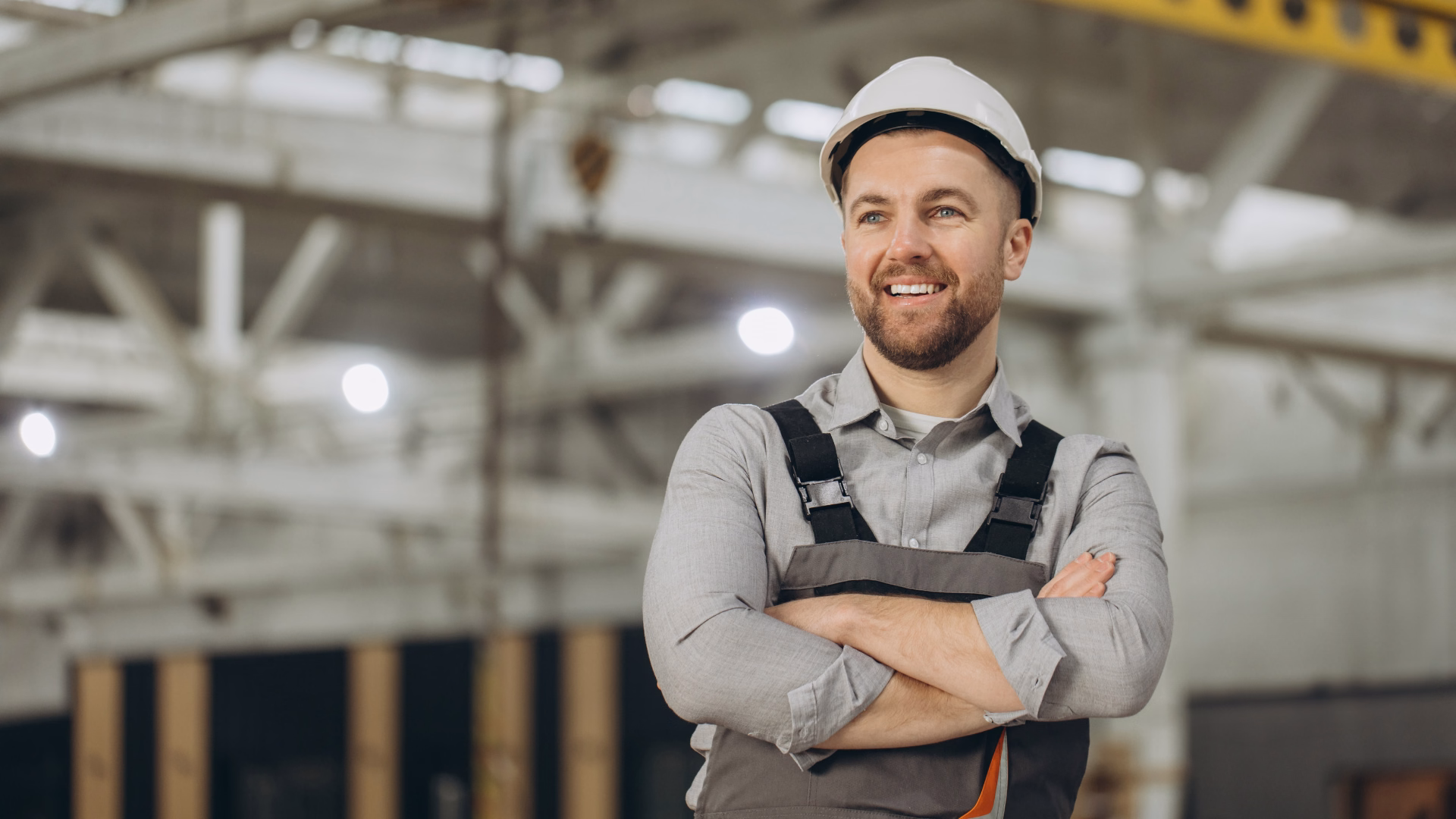 Lächelnder Ingenieur mit weißem Schutzhelm und grauem Overall steht stolz in einer modularen Baufabrik in Südwestsachsen - ITAS