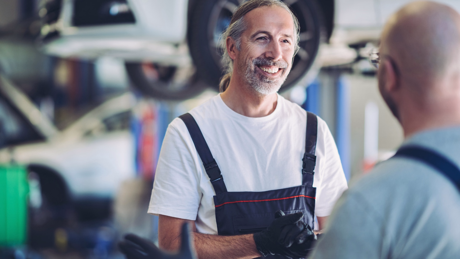 Lächelnde Automechaniker, die über die Arbeit in der Werkstatt sprechen in Südwestsachsen