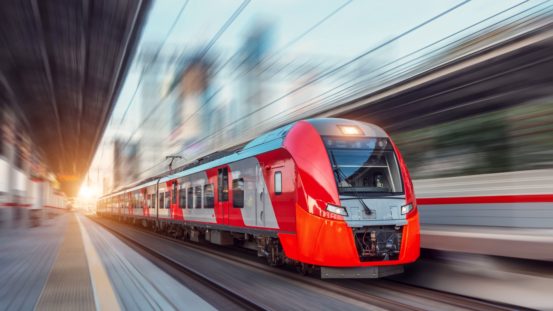 Ein elektrischer Personenzug fährt mit hoher Geschwindigkeit durch die Stadtlandschaft